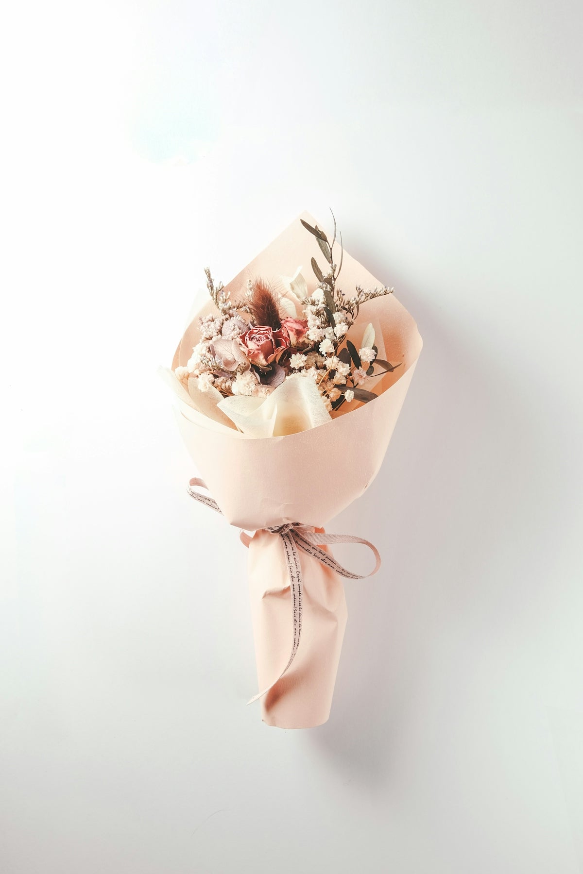 A bouquet of dried flowers wrapped in peach paper with a ribbon