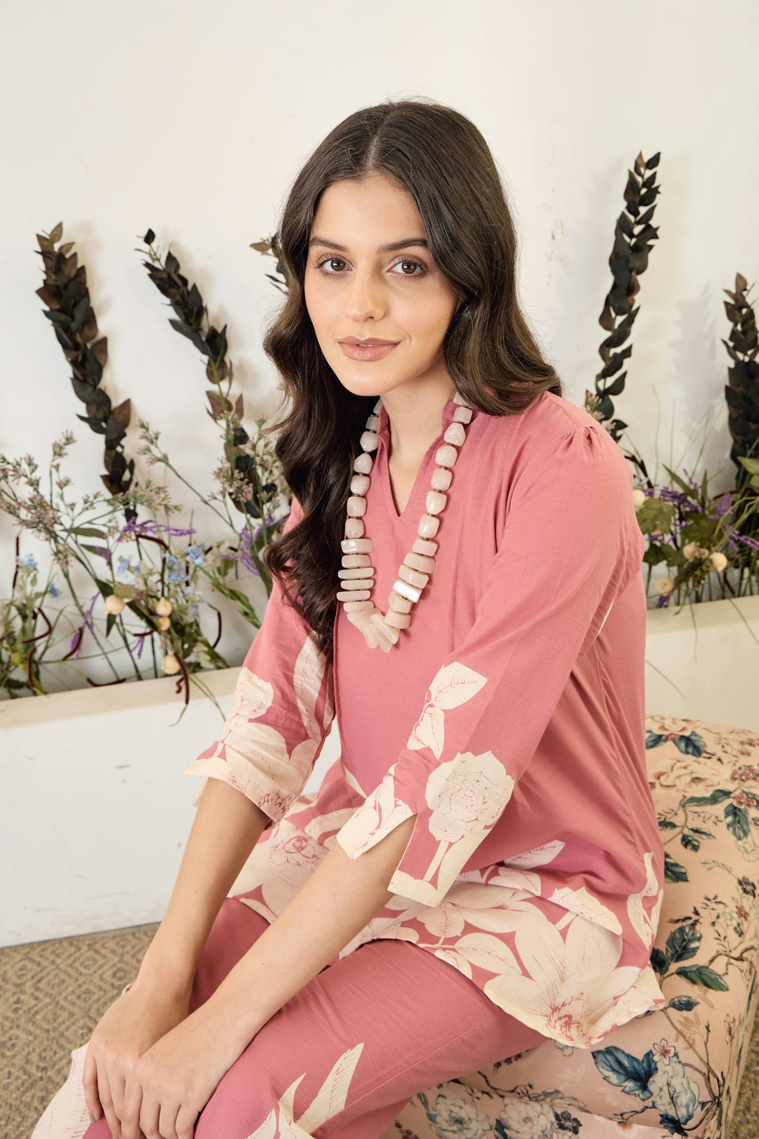 A woman wearing a pink floral outfit with a necklace.