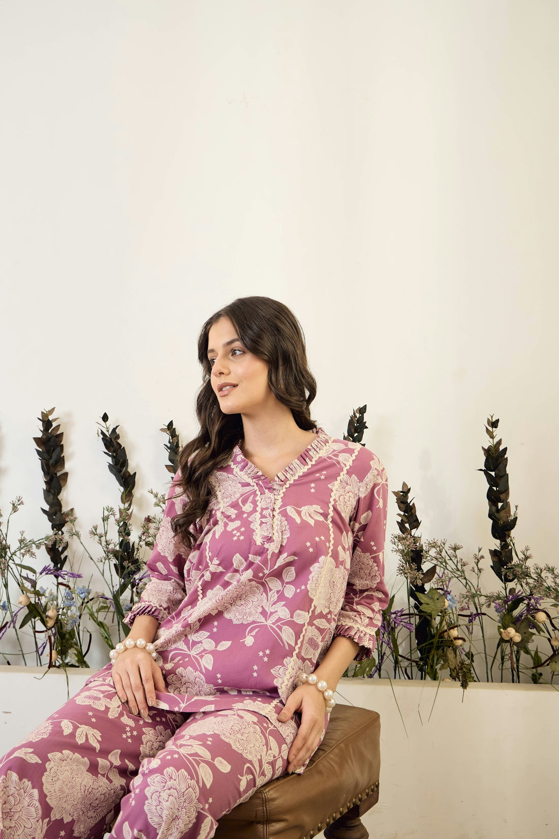 Woman in floral pajamas sitting on stool.