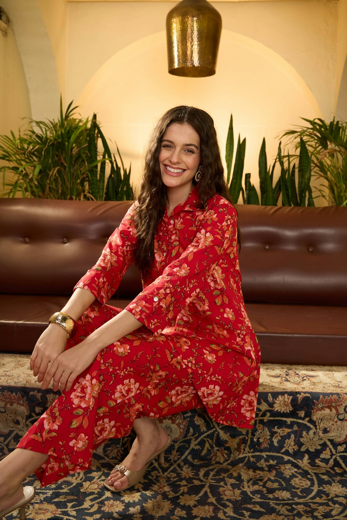 Smiling woman in red floral pajamas sits on couch.