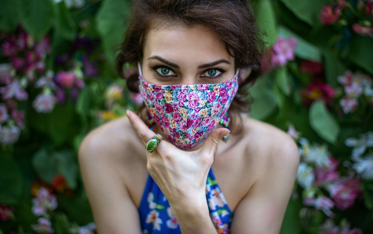 Woman wearing floral mask and ring against a flowery background.