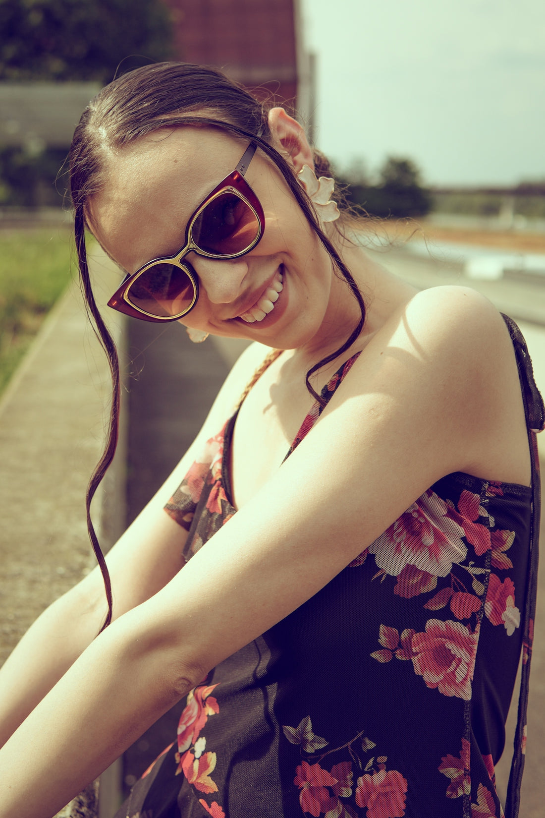 Happy woman in floral dress and sunglasses posing outdoors.