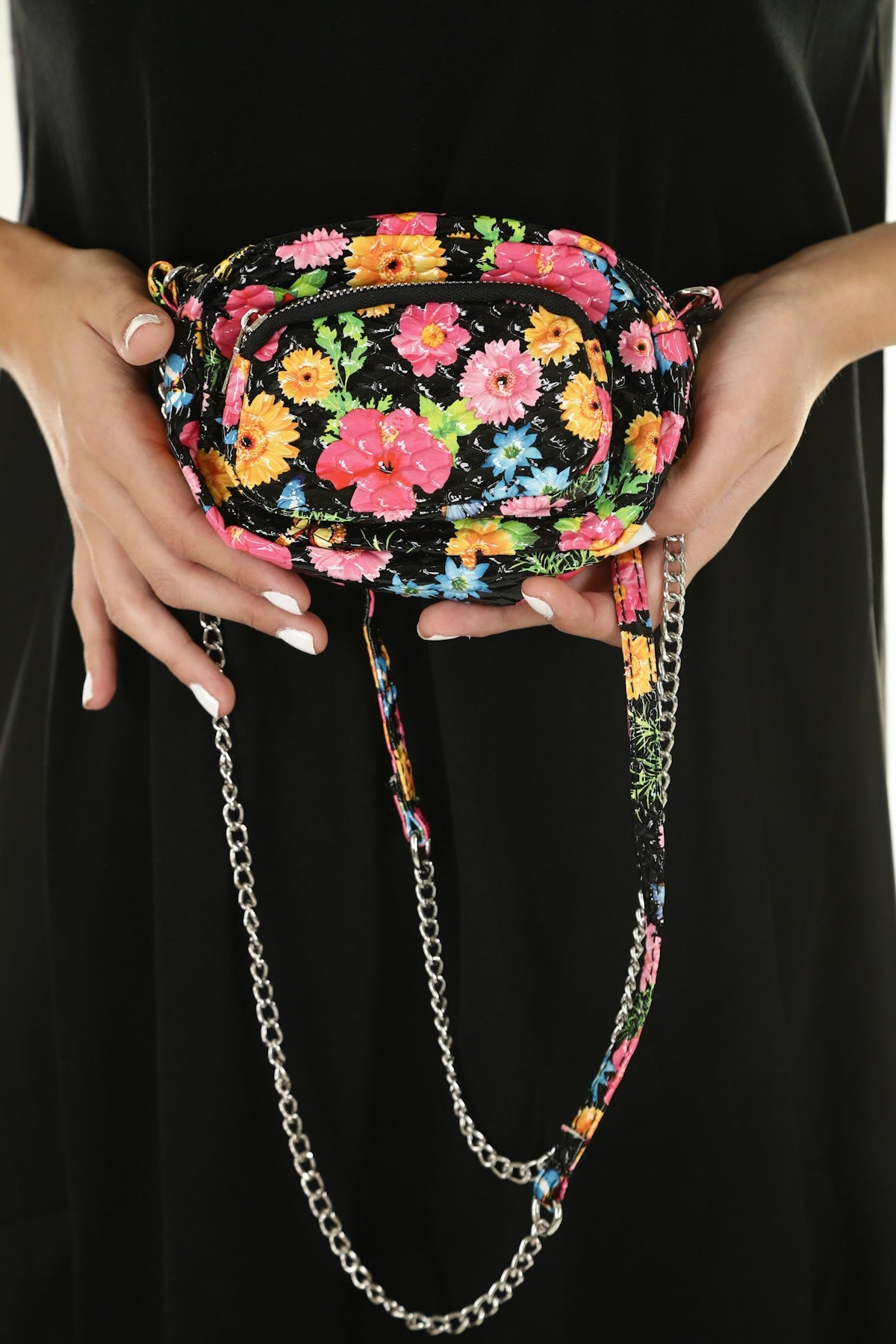 A person holding a small black floral handbag with a silver chain strap